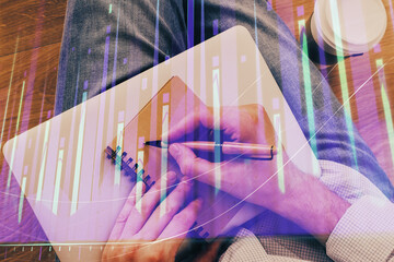 Double exposure of hands writing in notepad with stock market chart.