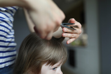 Woman doing haircut to child in an apartment. Mom cuts babys hair with scissors. Hairstyle for child at home. Buy scissors for beginning hairdresser. Hairdresser works with clients at home