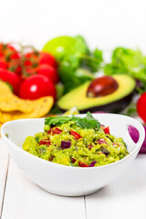 Bowl of Guacamole next to Fresh Ingredients on a Table with Tortilla Chips. Selective focus.