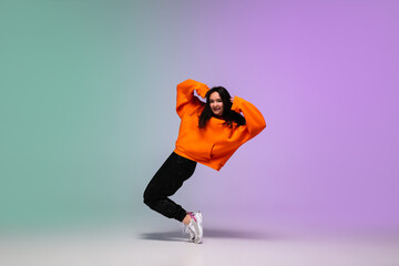 Beautiful sportive girl dancing hip-hop in stylish clothes on colorful gradient background at dance...