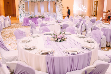 Banquet, restaurant. Table setting with tablecloth. White plates, cutlery, glasses, napkin, floral arrangements, food, chairs, flowers