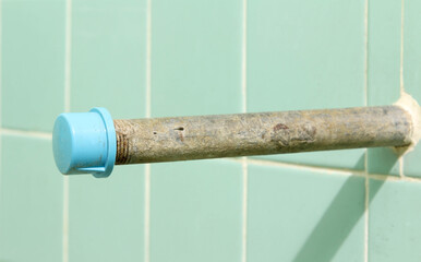 Plumbing steel dilapidated old rusty pipe on green tiles wall.