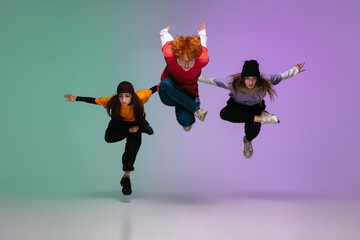 Group of teens, boys and girls dancing hip-hop in stylish clothes on colorful gradient studio...