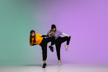 Fototapeta na wymiar Beautiful sportive girls dancing hip-hop in stylish clothes on colorful gradient background at dance hall in neon light. Youth culture, movement, style and fashion, action. Fashionable bright portrait