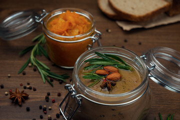 Glass jar with poultry pate, decorated with almonds and rosemary with orange jam on a wooden table