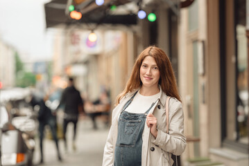 Fototapeta premium Beautiful young pregnant woman wearing casual clothes walking through the city streets. concept of motherhood and pregnancy. street portrait among cars close up view.