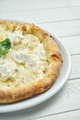 Appetizing, homemade 4 cheese pizza with blue cheese, mozzarella, parmesan and strachatella on a white plate on a white wooden background