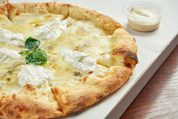 Photo for pizza delivery. 4 cheese pizza with blue cheese, mozzarella, parmesan and straccella in a cardboard box with side sauce on a wooden table