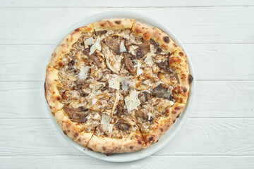 Appetizing, homemade pizza with different mushrooms, parmesan and white sauce on a white plate on a white wooden background