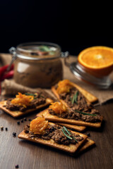 A few crackers with poultry liver pate and orange jam, hot pepper and orange fruits on the sackcloth and wooden background