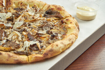 Photo for pizza delivery. Pizza with different mushrooms, parmesan and white sauce in a cardboard box with sauce for the sides on a wooden table