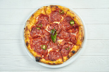 Appetizing homemade pizza with chorizo salami, hot pepper and melted cheese on a white plate on a white wooden background