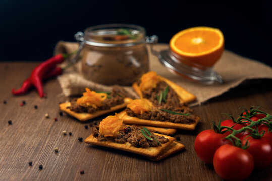 A few crackers with poultry liver pate and orange jam, hot pepper, cocktail tomatoes and sliced orange fruit on the sackcloth and wooden background