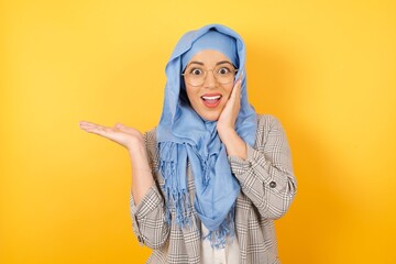 Positive young beautiful muslim woman wearing hijab says: wow how exciting it is, has amazed expression, indicates something One hand on her head and pointing with other hand. Advertisement concept.