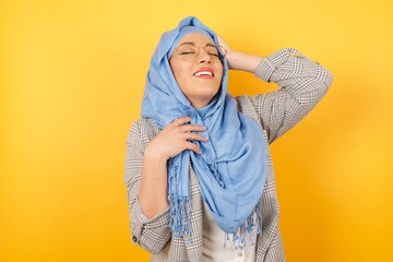 Shot of happy young muslim woman wearing hijab with positive smile, rejoices having weekend and good rest after hard working exhausting week, isolated on studio wall.