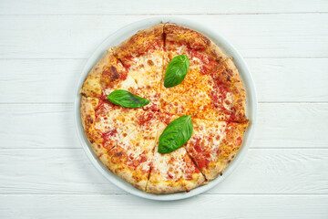 Appetizing, homemade pizza with margarita with tomatoes, basil and mozzarella on a white plate on a white wooden background. Close up