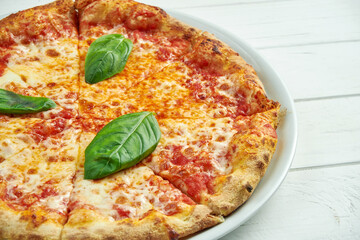 Appetizing, homemade pizza with margarita with tomatoes, basil and mozzarella on a white plate on a white wooden background. Close up