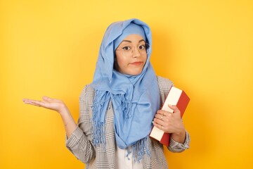 Puzzled and clueless young muslim woman wearing hijab with arms out, shrugging her shoulders, saying: who cares, so what, I don't know. Negative human emotions, facial expressions.