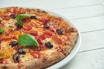 Appetizing, homemade pizza with margarita with cherry tomatoes, basil and mozzarella on a white plate on a white wooden background