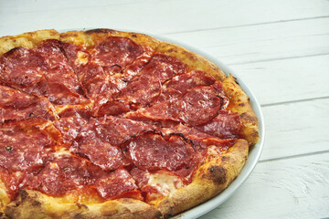 Appetizing, homemade pizza with salami, melted cheese and red sauce on a white plate on a white wooden background