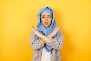 Young muslim woman wearing hijab and casual clothes standing over isolated background. Has rejection angry expression crossing hands doing refusal negative sign.