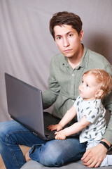 young man working at home with a laptop with a baby on his hands. Stay home concept. Home office with kids.