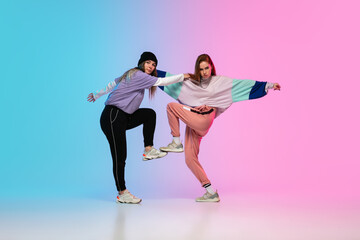 Flexible. Sportive girls dancing hip-hop in stylish clothes on colorful gradient background at...