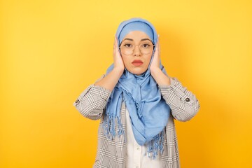 Young muslim woman wearing hijab plugging ears with hands does not wanting to listen rock or loud music, ignoring noise covering her ears with hands avoiding loud sounds at street.