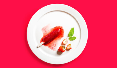 Delicious defrosted strawberry popsicles on white round dish over red background