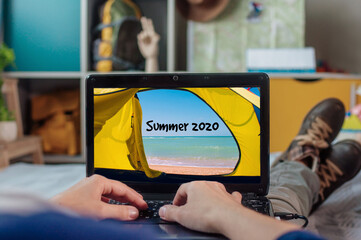 Young woman laying and holding laptop with inspirational photo and inscription SUMMER 2020 in the...