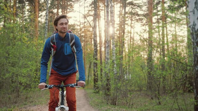 Active young man riding bike on forest trail at sunset, enjoying nature