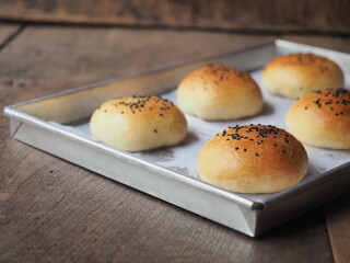 Brioche bread bun with black sesame seed topping on baking tray