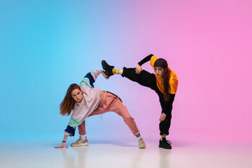 Flexible. Sportive girls dancing hip-hop in stylish clothes on colorful gradient background at...