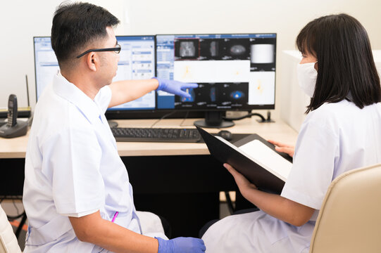 Asian radiologists shows the patient CT scan image at display for explaining and discussion treatment patient information to doctor in x-ray room.