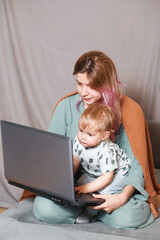 A young woman works at home with a laptop, along with a child.the son wants to communicate with his...
