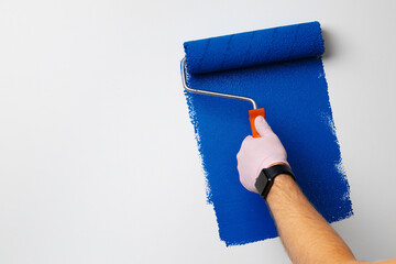 Gloved male hand painting wall into classic blue color
