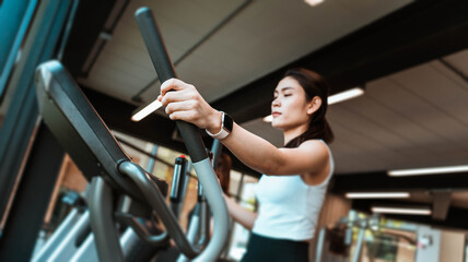 Young fitness girl walking on the elliptical machine at the gym