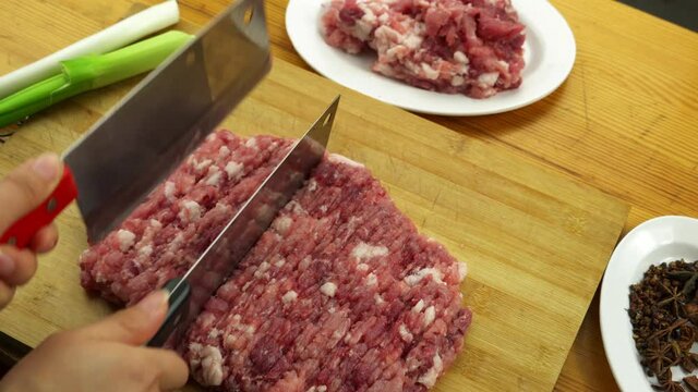 Closeup, two kitchen knives chopping minced meat on cutting board, leek and seasoning