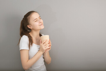 Aromatic coffee in a glass. Young woman drinks hot drink on gray background