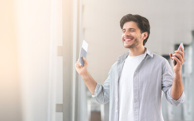 Happy Man Standing In Airport, Holding Passport With Tickets And Smartphone