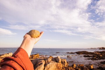 Hand pointing to the horizon against a blue sky, with the sea and the coast in the background
