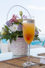 Alcoholic drink with fruit juice in glass and a basket of flowers, blur background
