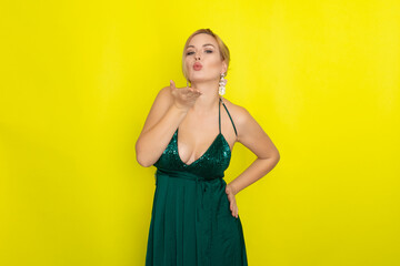 Blond woman wearing green evening dress over yellow background