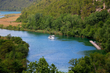 Aerial view of river Krka with tourist boat and nearby forest. Entrance to National Park Krka, Croatia.