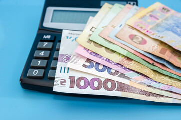 different hryvnias on a calculator. Blue background. Close-up. Savings concept.
