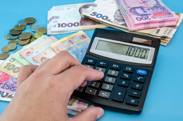 hand prints on a calculator on the background of different hryvnia and coins. Blue background. Close-up. Revenue analysis, financial concept.