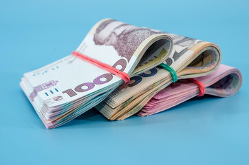 1000, 500, 200 hryvnia bound by an elastic band isolated on a blue background. Close-up. Hryvnias rolled into a roll