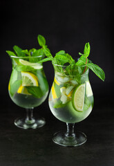 Summer mint lime refreshing cocktail mojito with rum and ice in glass on black background. Mojito cocktail on dark stone table. Glassy high glass for drinks. Lemonade at the bar.
