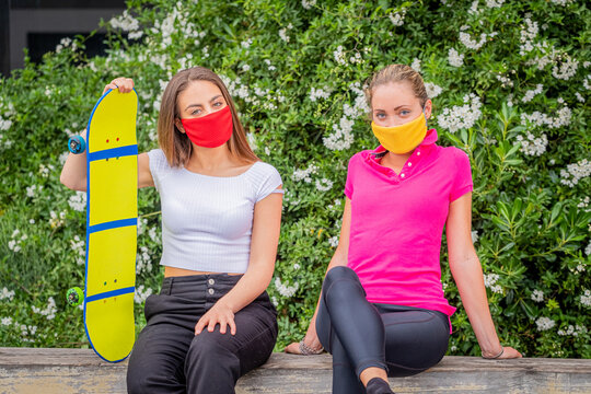 Portrait of two beautiful girls while are sitting and are speaking with protective mask during quarantine time for pandemic covid19  - Friends are sitting with skateboard in relaxing time