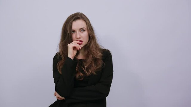 Young Attractive Woman Brunette In In A Black T-Shirt, Sweater On White Background, Focused Female Holds Finger Near Her Mouth And Thinks. The Concept Of Smart People, Intellectuals